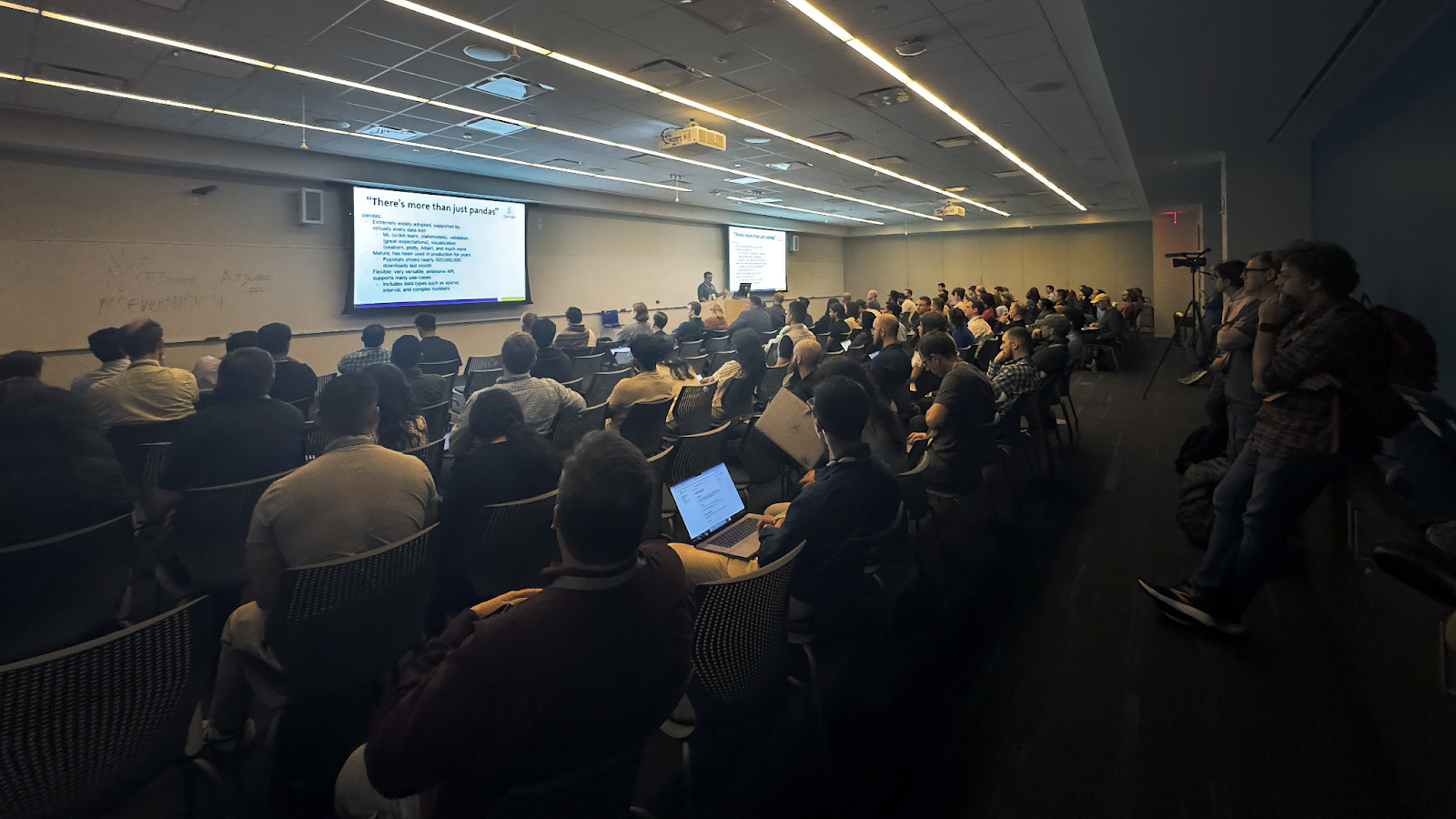 Dharhas Pothina presenting at PyData NYC on November 7, 2024 to a full room of attendees, discussing modern DataFrame tools such as pandas, Polars, and DuckDB. The presentation slide on the screen reads 'There's more than just pandas' and highlights key features of pandas.