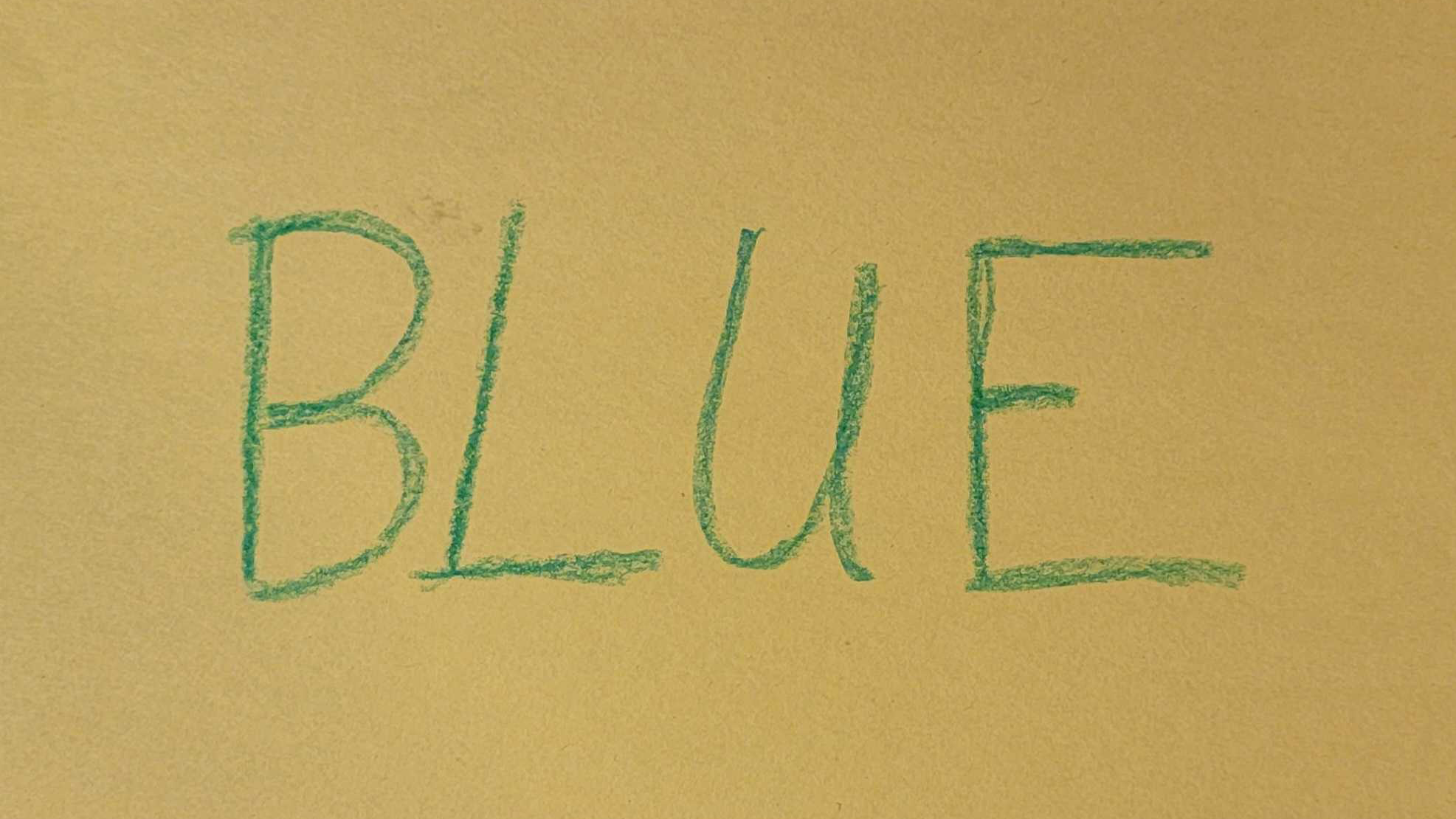 An image of yellow paper with the word BLUE written in green colored crayon