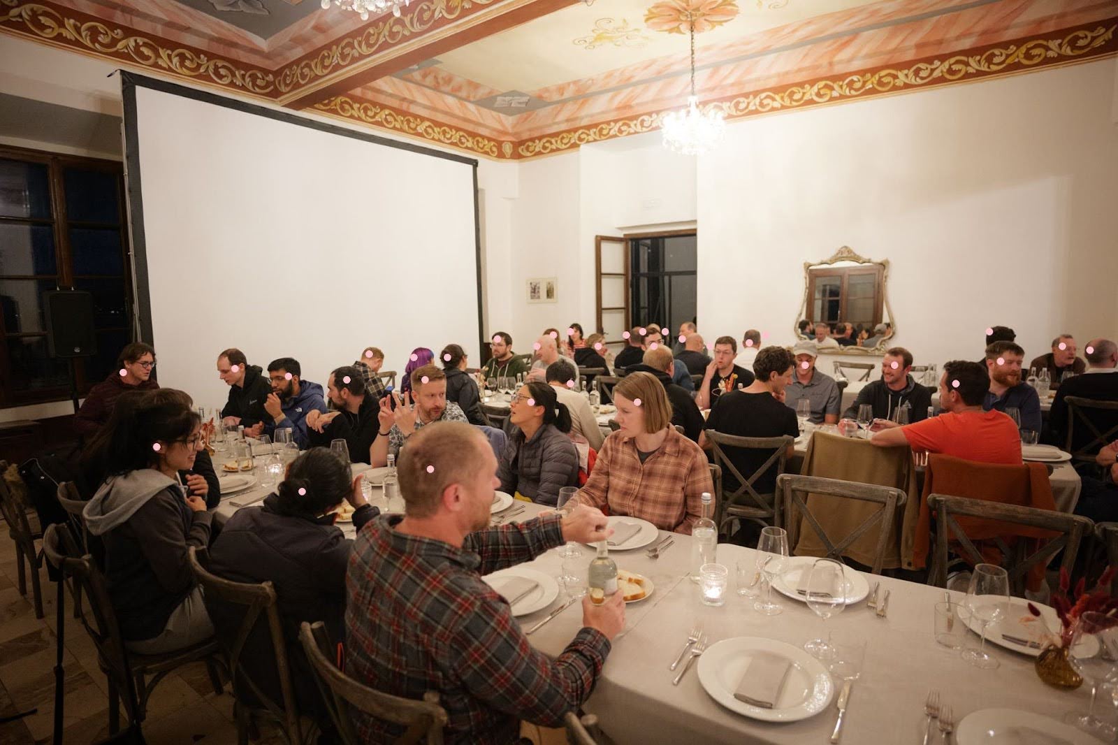 Group dinner scene in a warmly lit room with decorative ceilings and a large blank